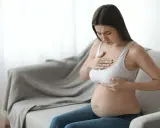 Ciężarna kobieta z bólem dotyka piersi, czując pierwsze oznaki siary.