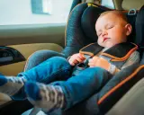 Małe dziecko śpi w foteliku samochodowym, jego opadająca głowa w foteliku świadczy o głębokim śnie podczas podróży.
