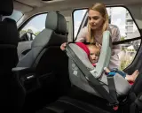 Mama pokazuje, jak zapiąć fotelik pasem, by bezpiecznie przewieźć malucha.