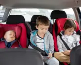 Dziecko śpi w foteliku, a dwaj starsi bracia grają na telefonach. Od kiedy można zapinać dziecko pasami samochodowymi? Od urodzenia, w odpowiednim foteliku.
