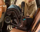 Mężczyzna wyjmuje fotelik z isofix z samochodu. Widać uchwyt i koła fotelika.