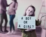 Dziewczynka trzyma tabliczkę "A BOY OR A GIRL?". Rodzice czekają na dziecko, a płeć można poznać do 20. tygodnia ciąży.