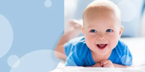 Uśmiechnięte dziecko z niebieskimi oczami, kiedy dziecko trzyma głowę na brzuchu, leżąc na białym tle.