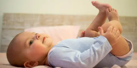 5-miesięczne dziecko leży na plecach, podnosząc nóżki i bawiąc się nimi. To pokazuje, co potrafi 5 miesięczne dziecko.