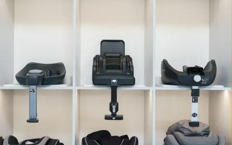 Trzy różne modele bazy isofix prezentowane na półkach. Każda baza jest czarna, z elementami montażowymi.