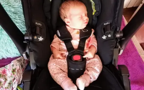 Śpiący noworodek w różowym pajacyku z króliczkami w foteliku Kiddy. Wkładka noworodkowa zapewnia komfort i bezpieczeństwo.