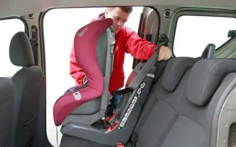 Mężczyzna montuje fotelik samochodowy. Sprawdź, jak sprawdzić, czy samochód ma isofix, patrząc na zaczepy fotelika.