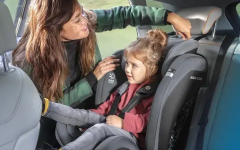 Mama poprawia zagłówek w foteliku samochodowym 9-36 dla swojej córki.