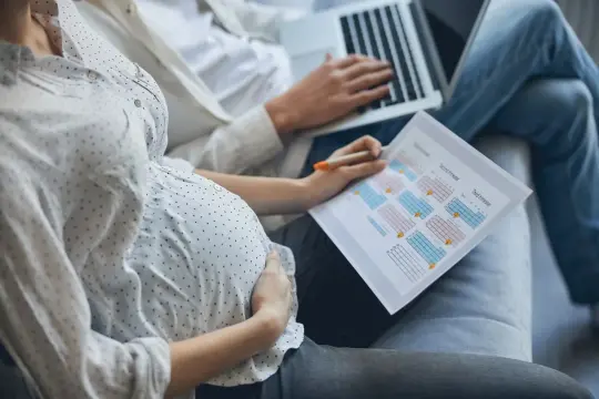 Kobieta w ciąży z partnerem planuje tygodnie ciąży a miesiące, analizując harmonogram na papierze.
