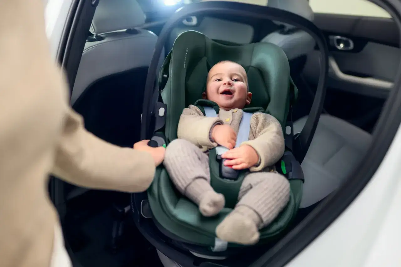 Uśmiechnięte dziecko w foteliku samochodowym na bazie do Maxi Cosi. Bezpieczna podróż dla malucha.
