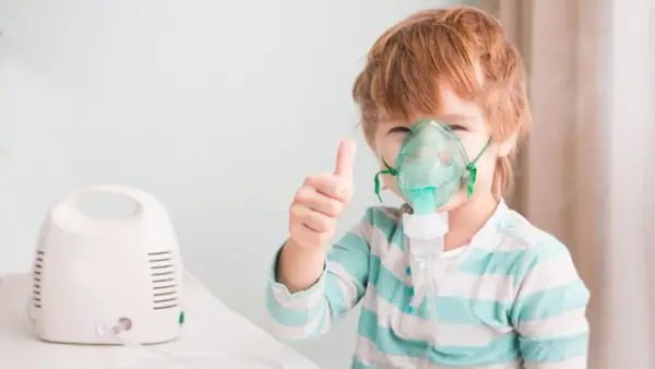 Chłopiec z gorączką i przyspieszonym oddechem używa nebulizatora, pokazując kciuk w górę.