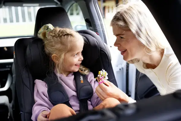 Uśmiechnięta mama daje córeczce w foteliku samochodowym bukiecik kwiatów. To miły test plus dla małej pasażerki.